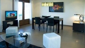Una habitación de hotel moderna con una mesa de comedor de cristal, un televisor y un sofá.