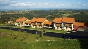 Una hilera de casas con techos rojos, enmarcada por colinas verdes y un cielo despejado.