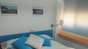 A bedroom with a blue headboard, a bed with blue and white bedding, a bedside table with a lamp, and two framed pictures on the wall. - Nevada Apartaments, between Granada and Sierra Nevada (Cenes de la Vega)
