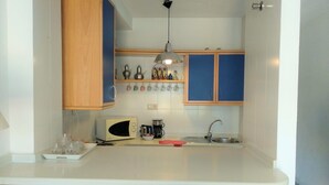 A compact kitchen with wooden cabinets, a white countertop, a microwave, a kettle, and a sink. - Nevada Apartaments, between Granada and Sierra Nevada (Cenes de la Vega)