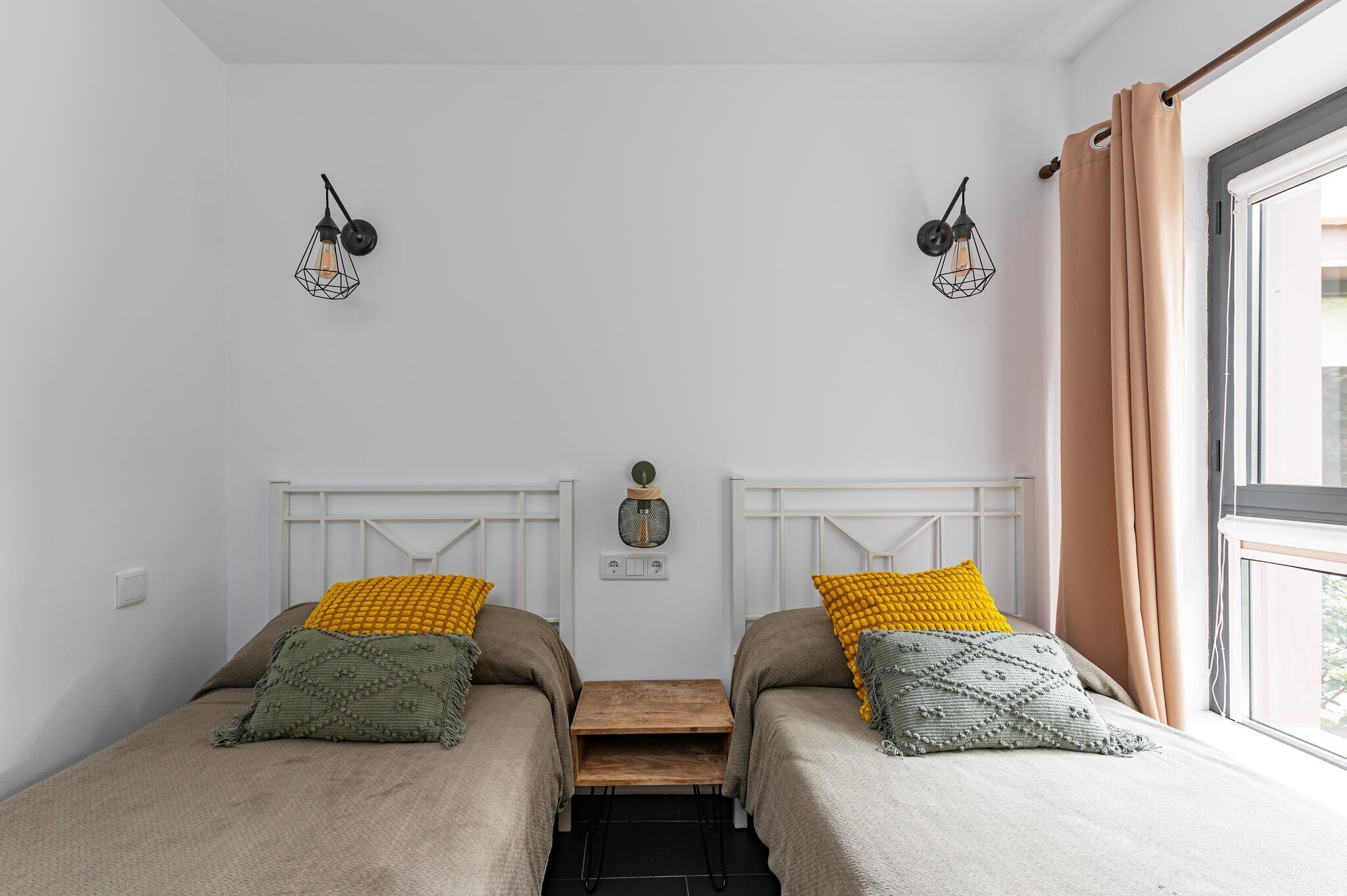 Une chambre avec deux lits, une petite table en bois et deux appliques murales.