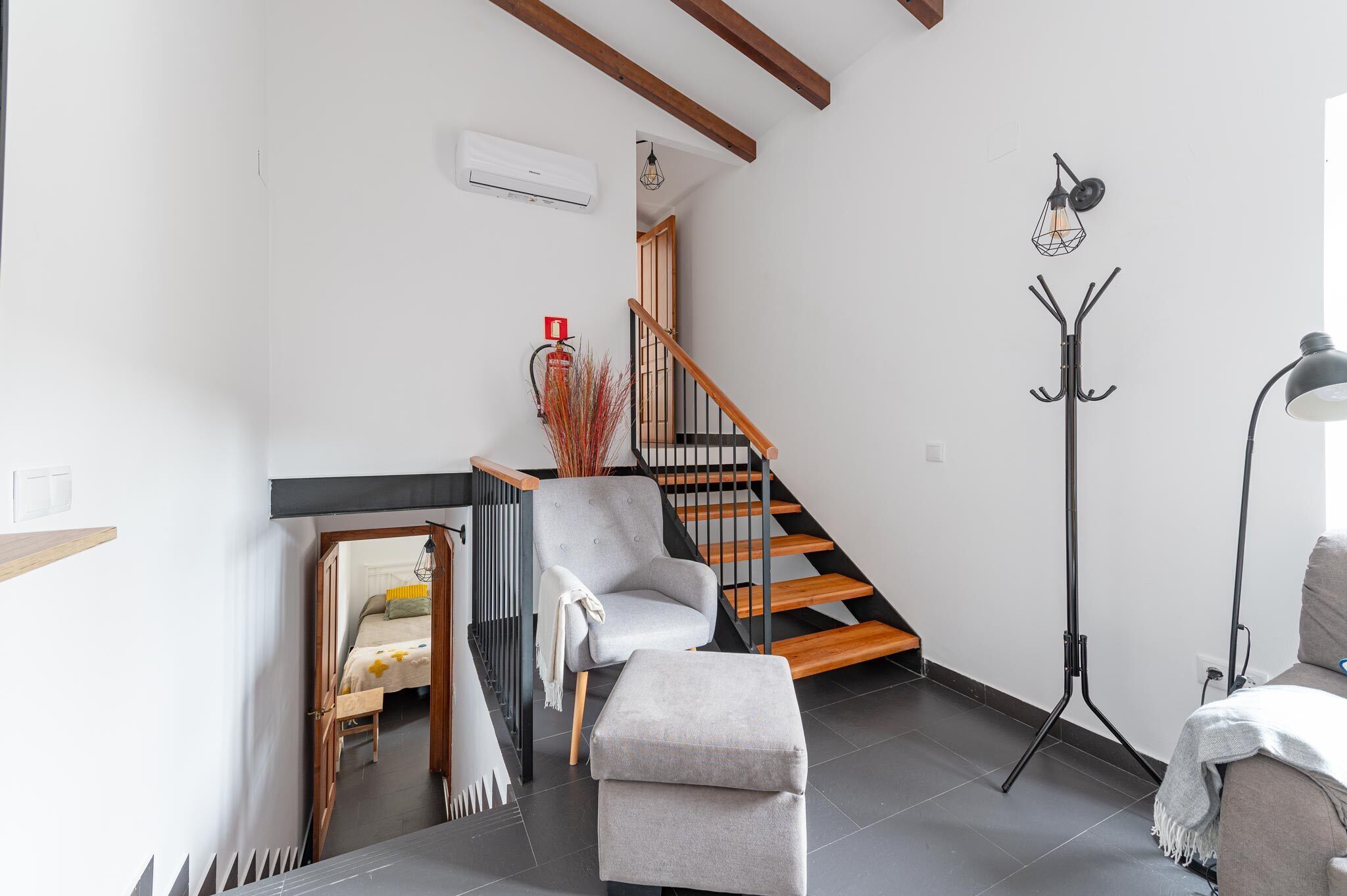 A modern living room with a grey sofa, a wooden staircase, a floor lamp, and a small table with a lamp.
