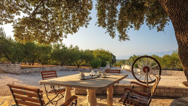 An outdoor dining area with a table, chairs, and a decorative wheel. - Secluded Villa Dubrava, private pool, olive grove surrounds the villa, Brac Island (Pučišća)