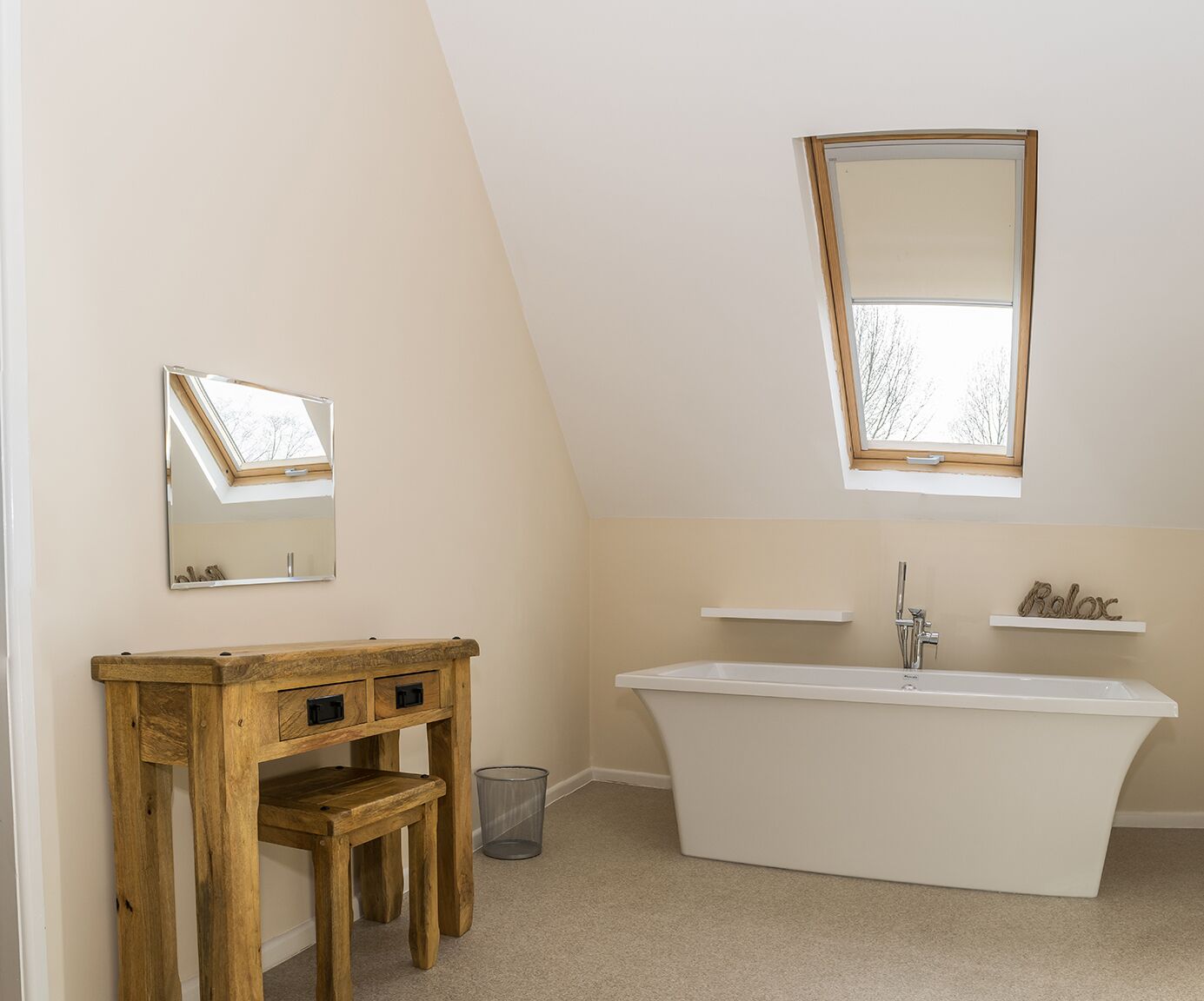 A bathroom with a freestanding bathtub, a wooden vanity, a mirror, and a window.