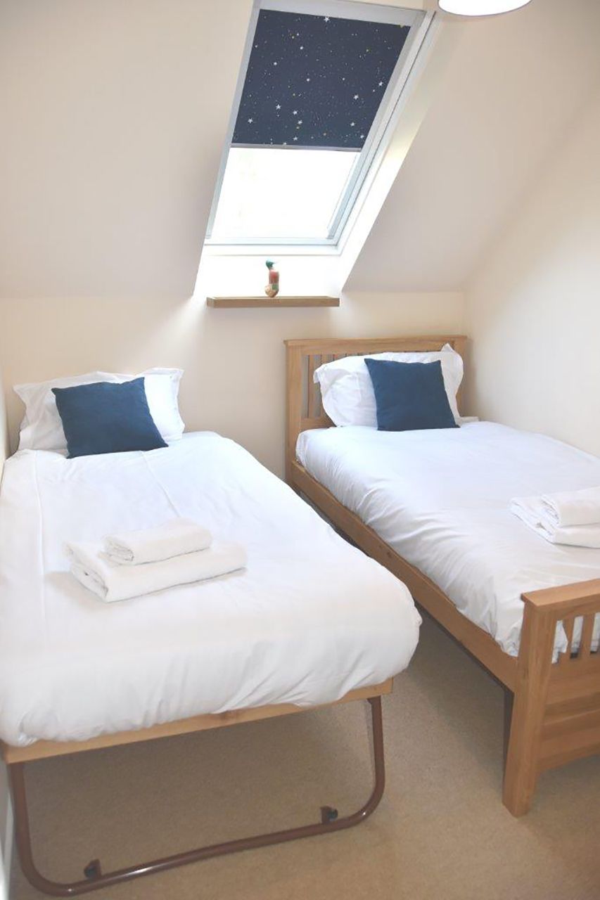 Une chambre double avec deux lits simples, une lucarne et une petite étagère avec une plante.