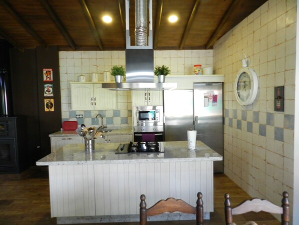 Cozinha com ilha central, eletrodomésticos de aço inoxidável e teto de madeira.