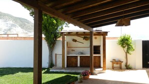 A covered outdoor patio with a wooden pergola, a barbecue area, and potted plants.