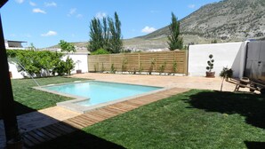 A backyard with a rectangular swimming pool, a wooden deck, and a grassy lawn.