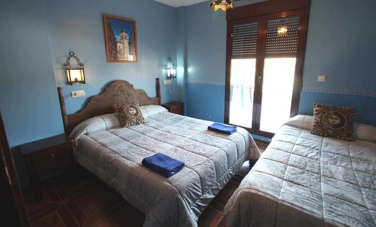 Un dormitorio con dos camas, una mesita de noche, una lámpara de pared y una ventana con persianas.