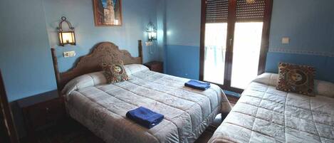 A bedroom with two beds, a nightstand, a wall-mounted lamp, and a window with blinds.