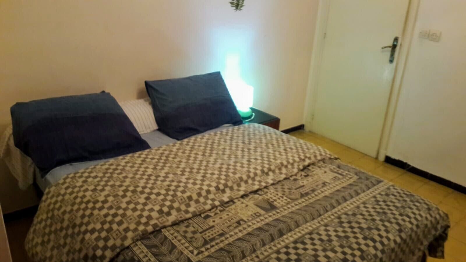 A bed with patterned bedding, a bedside lamp, and a door to the right.