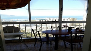 Ein Balkon mit Tisch und Stühlen mit Blick auf eine Stadtlandschaft und das Meer.