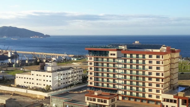 Ein mehrstöckiges Hotel mit modernem Design, nahe einem Hafen mit Industriegebäuden und Blick auf das Meer.