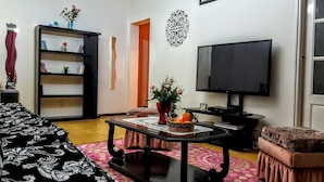 Ein Wohnzimmer mit einer Couch, einem Couchtisch mit Dekoration, einem Bücherregal, einem Fernseher und einem gemusterten Teppich.