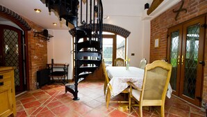 A dining area with a spiral staircase, a table with chairs, and a brick wall. - Coach House at Oaks Barn Farm, optional salt water hot tub near to Stratford. (Alcester)