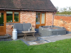 Een terras met een bakstenen muur, een jacuzzi, een bank en een tafel met fles en glas.