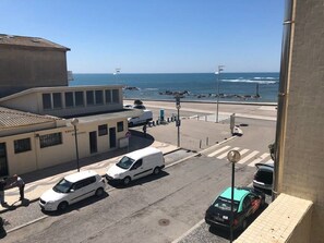 Une rue côtière bordée de voitures garées, un bâtiment portant l’inscription « Mercado de la Playa », et une vue sur l’océan.