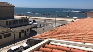 Vista costera desde un edificio con tejas de arcilla, un estacionamiento y una carretera que lleva a la playa.