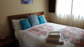 Uma cama bem arrumada com um edredom estampado, duas almofadas e uma toalha dobrada sobre a cama.