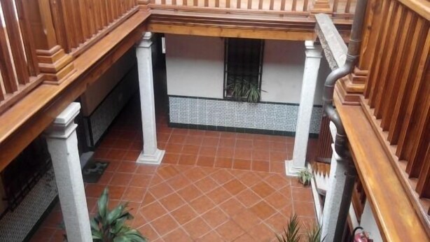 Uma varanda de madeira com soalho em azulejos, pilares brancos e uma pequena janela.
