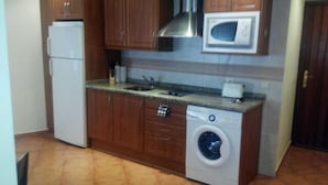 Uma cozinha compacta com armários de madeira, micro-ondas embutido, máquina de lavar e frigorífico.