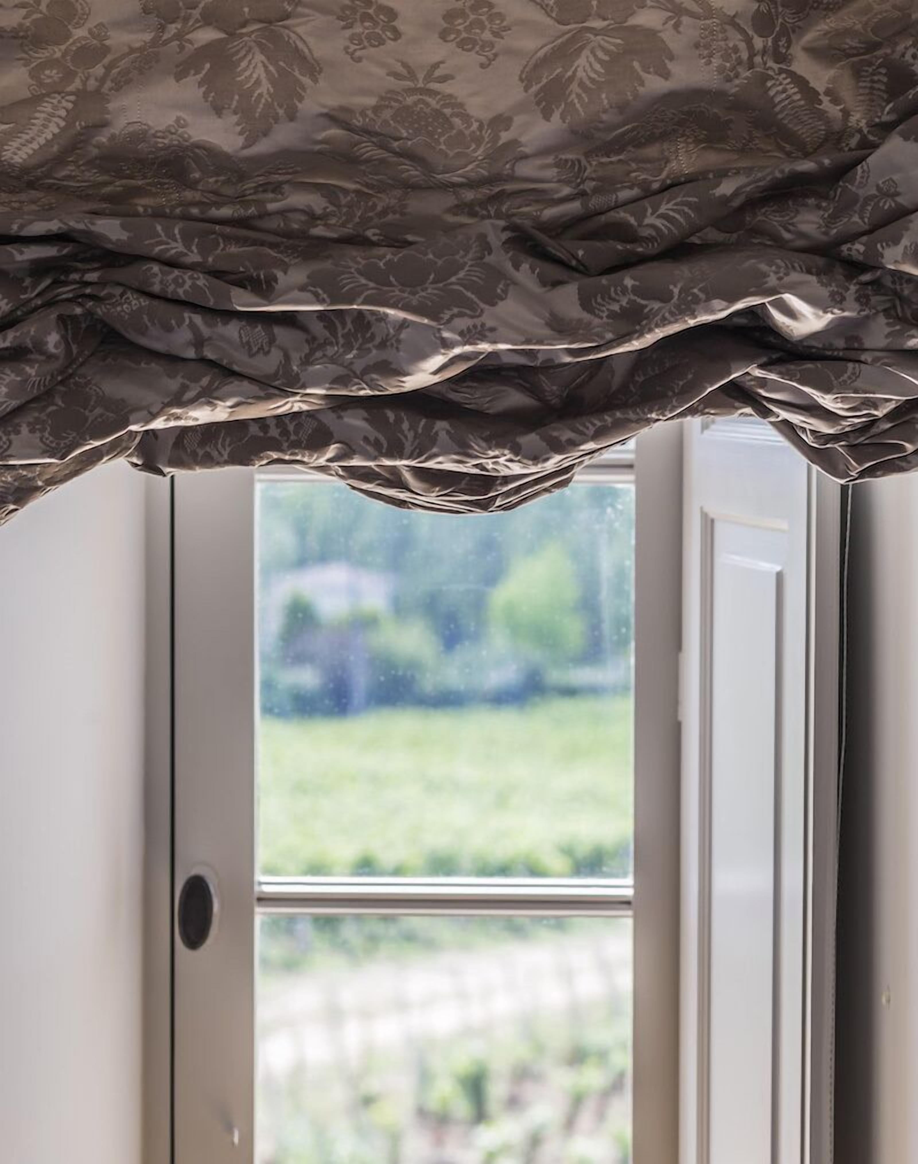 Ein Fenster mit einem gemusterten Vorhang und Blick auf eine grüne Landschaft.