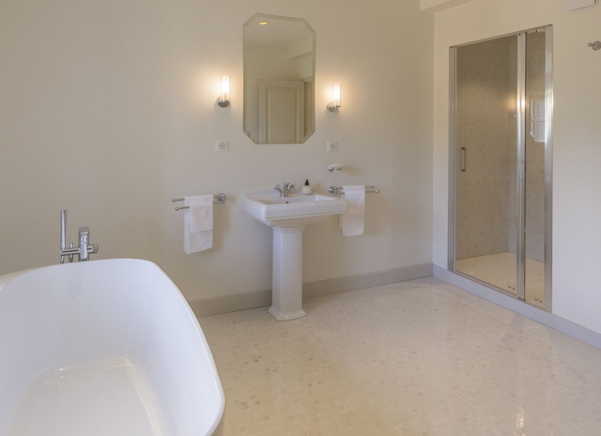 A bathroom with a freestanding bathtub, a pedestal sink, a large mirror, and a glass-enclosed shower.