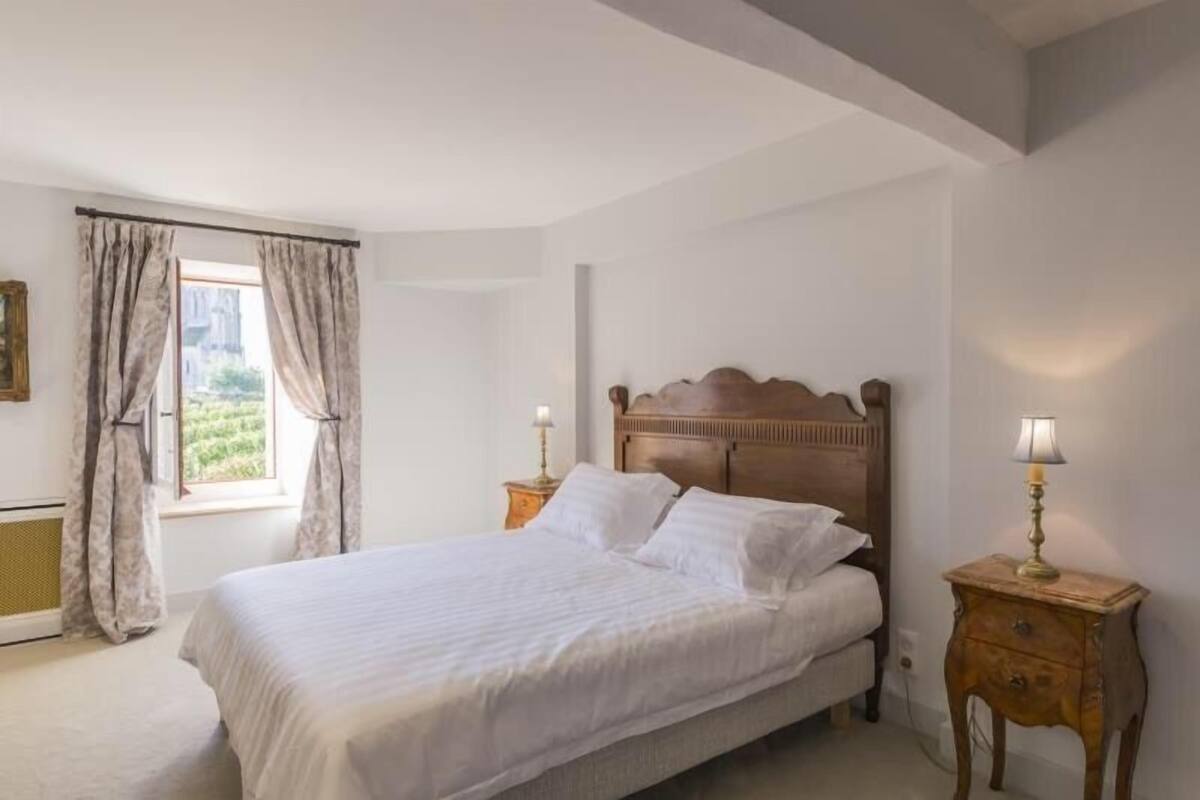 Une chambre à coucher avec un grand lit, une table de chevet avec une lampe et une fenêtre avec des rideaux.