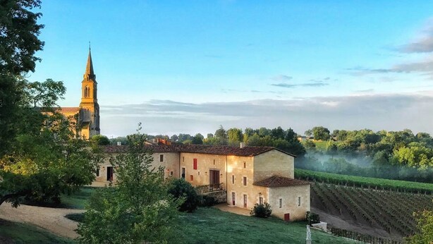Ein historisches Gebäude mit einem Kirchturm, umgeben von üppiger Vegetation und einem Weinberg.