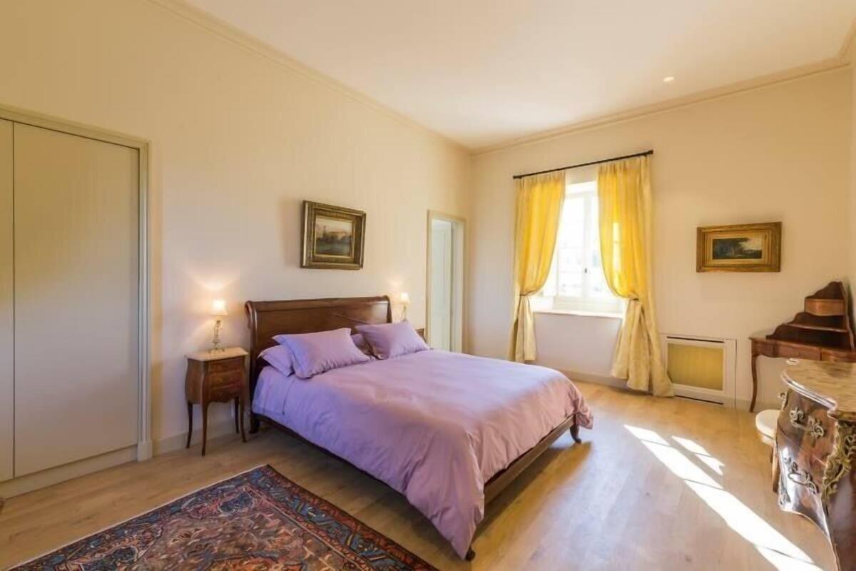 Une chambre à coucher avec un lit en bois, une table de chevet, une commode et une fenêtre avec des rideaux.