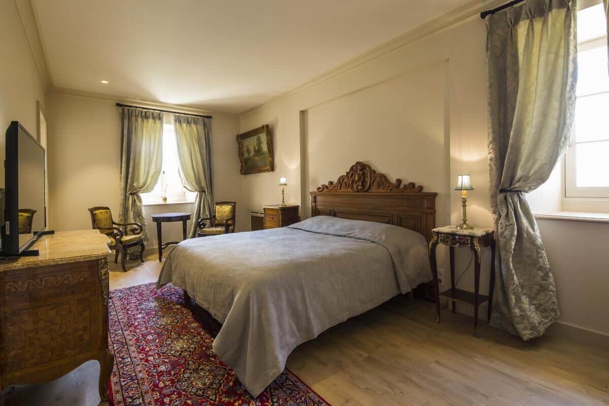 Une chambre à coucher avec un lit, une commode, une chaise, une table et une fenêtre avec des rideaux.