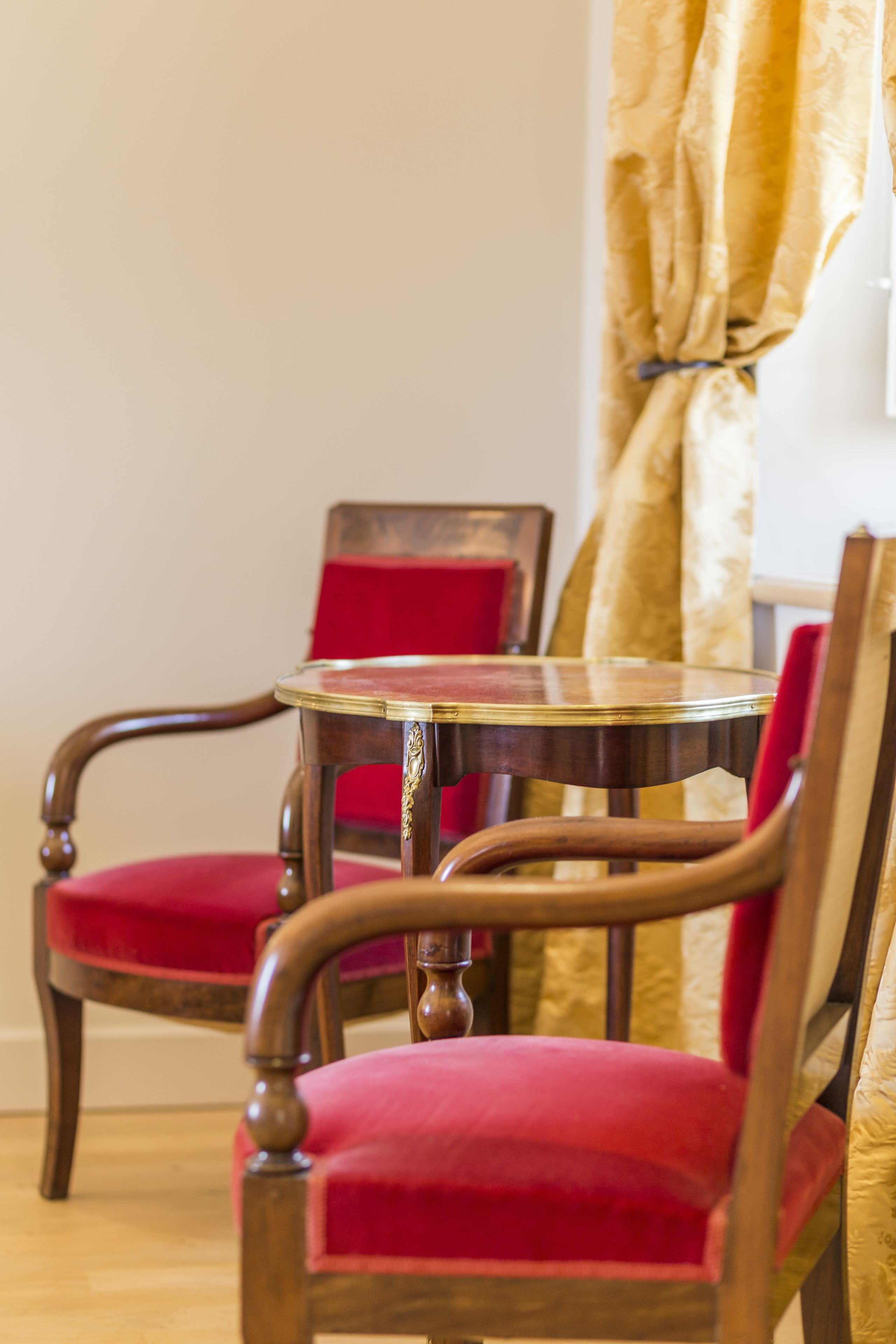 Un comedor con una mesa redonda de madera y dos sillas tapizadas rojas.
