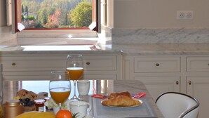 Ein Frühstückstisch mit Croissants, Obst und Orangensaftgläsern, vor einem Fenster mit Blick auf eine bewaldete Landschaft.