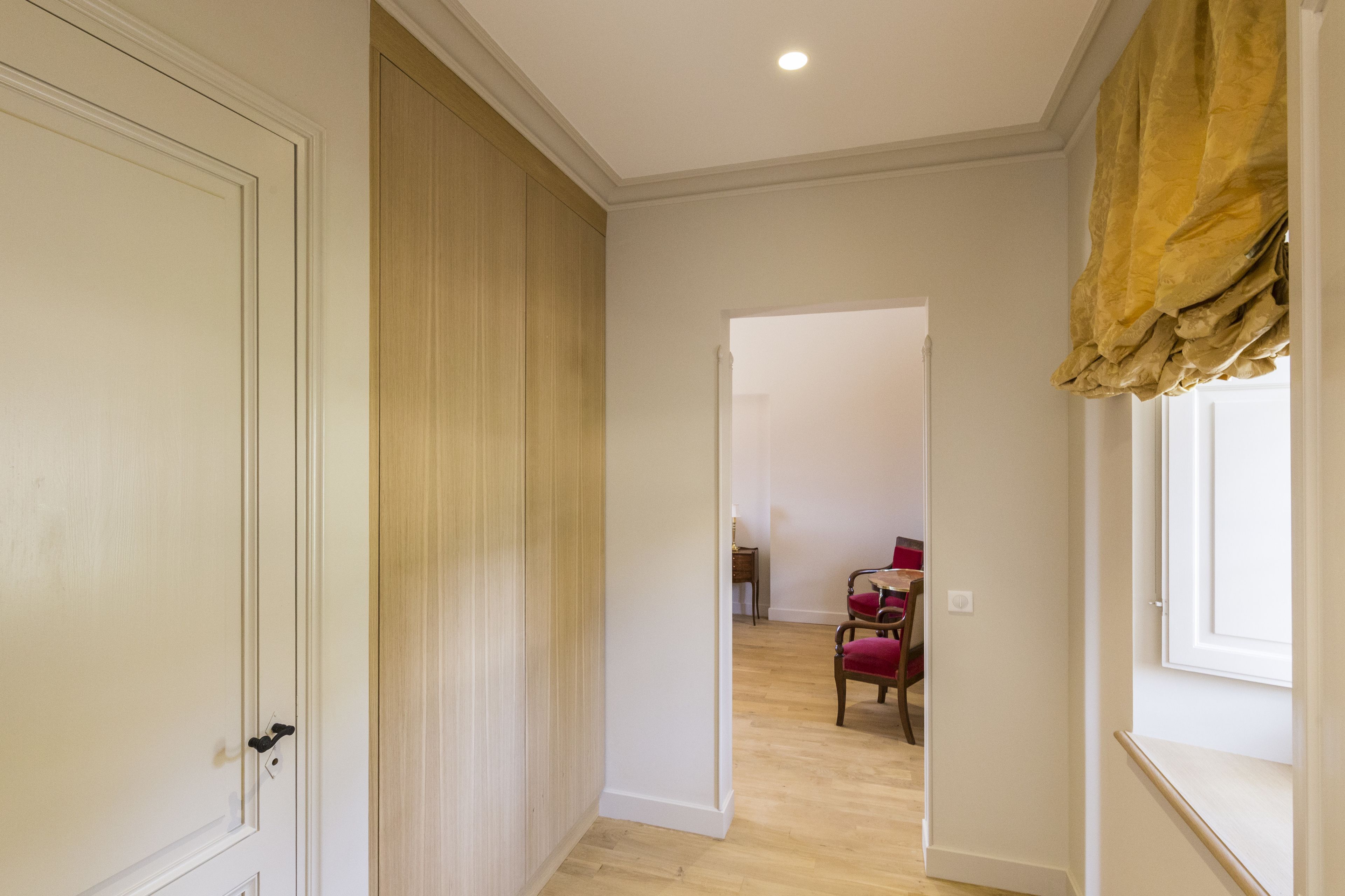 A hallway with a wooden floor, a door on the left, and a window on the right.