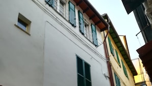 Een smalle straat met gebouwen in traditionele stijl, waaronder een wit gebouw met groene luiken en het zichtbare nummer 21.