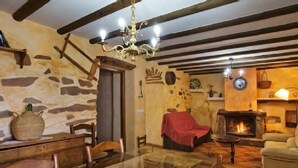 A rustic interior with exposed wooden beams, a stone wall, a fireplace, and a dining area with a glass table. - Rural house (rental entire) Reul Alto Cortijos Rurales for 6 people (Laroya)