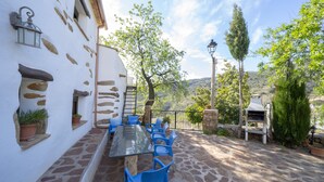 An outdoor patio with a long table and blue chairs, surrounded by stone walls and potted plants. - Rural house (rental entire) Reul Alto Cortijos Rurales for 6 people (Laroya)