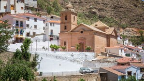 A hillside town with a prominent church featuring a bell tower, surrounded by white and red buildings with terracotta roofs. - Rural house (rental entire) Reul Alto Cortijos Rurales for 6 people (Laroya)