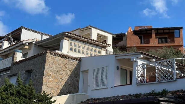 A multi-story residential building with a stone facade, a white upper level with a balcony, and a red lower level.