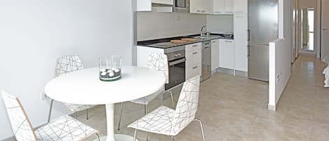 Una cocina moderna con armarios blancos, un refrigerador de acero inoxidable y un comedor con mesa y sillas blancas.