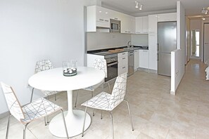 Une cuisine moderne avec des meubles blancs, un réfrigérateur en acier inoxydable et un coin repas comprenant une table et des chaises blanches.