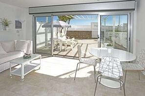 A modern living room with a white sofa, a glass-top table, and a dining area with chairs and a table. - Chalet Mare Nostrum (Maspalomas)