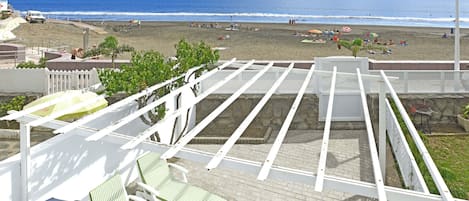 A rooftop terrace with white railings, green striped lounge chairs, and a view of the beach and ocean.