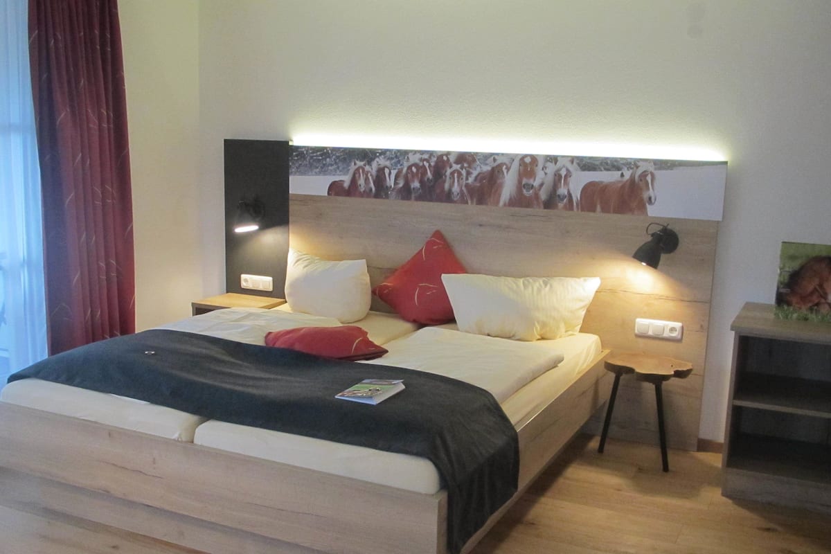 A neatly made bed with a headboard, a bedside table, a lamp, and a wall-mounted picture.
