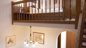 A loft bedroom with a wooden balcony railing, a dining area with a chandelier, and a staircase.