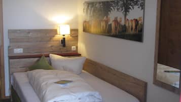A neatly made bed with a green upholstered headboard, a bedside lamp, and a painting of horses on the wall.
