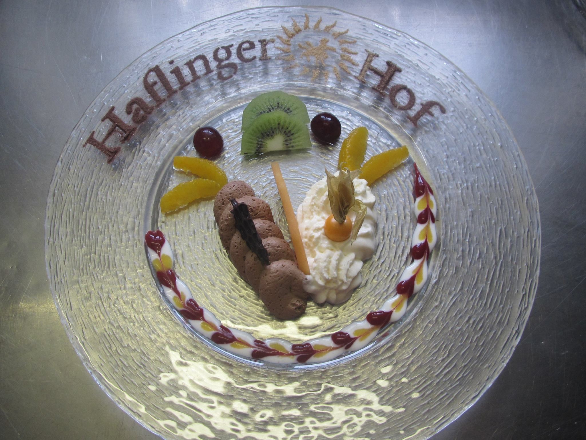 A clear glass dessert plate with a decorative border, featuring a variety of fruits and a chocolate piece.