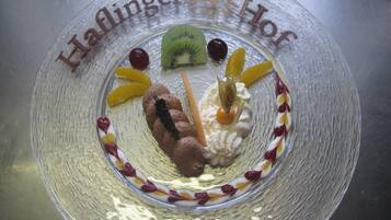 A clear glass dessert plate with a decorative border, featuring a variety of fruits and a chocolate piece.