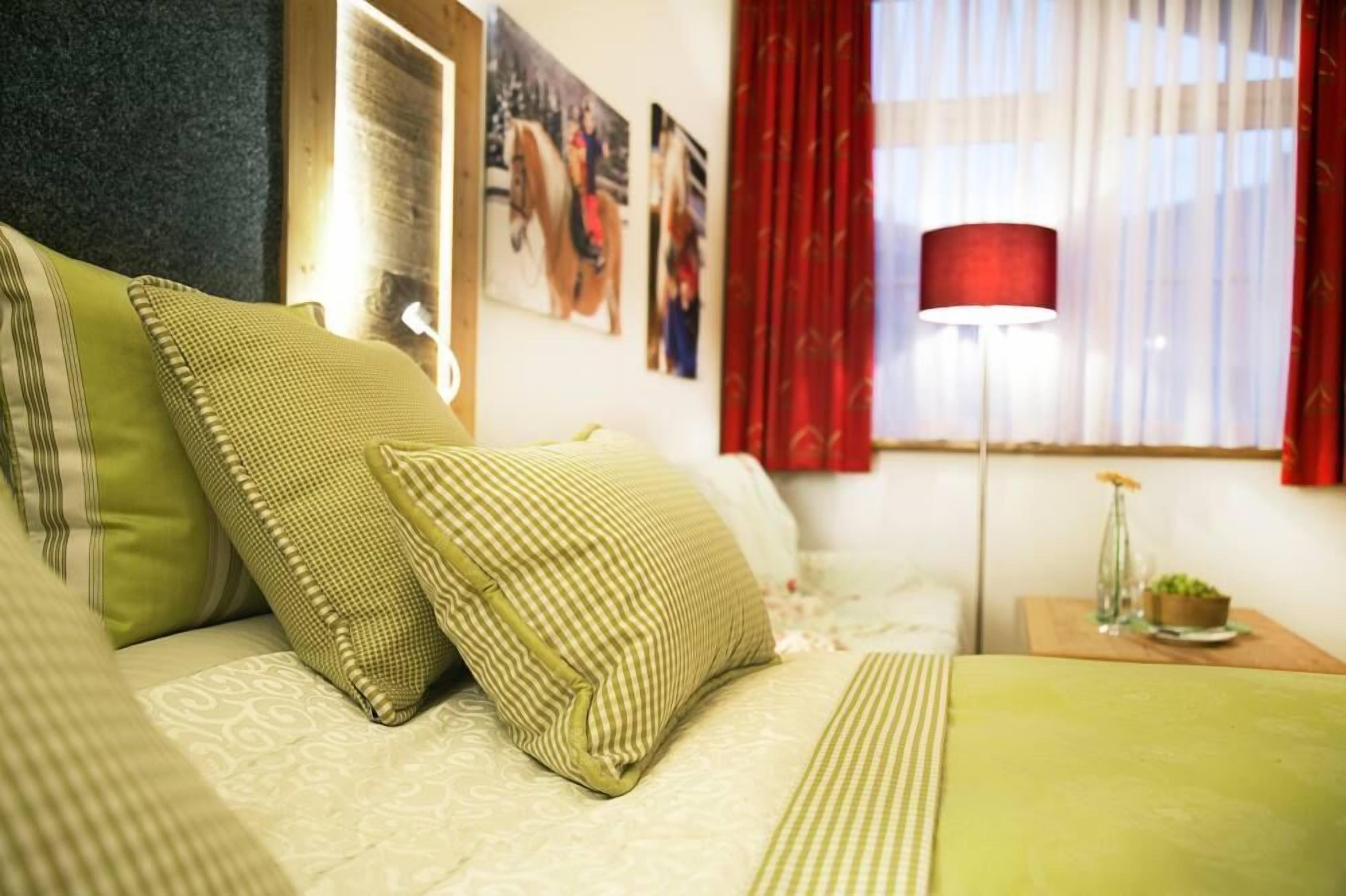 Ein Hotelzimmer mit Bett, Kissen, einem Nachttisch mit Lampe und einem Fenster mit roten Vorhängen.
