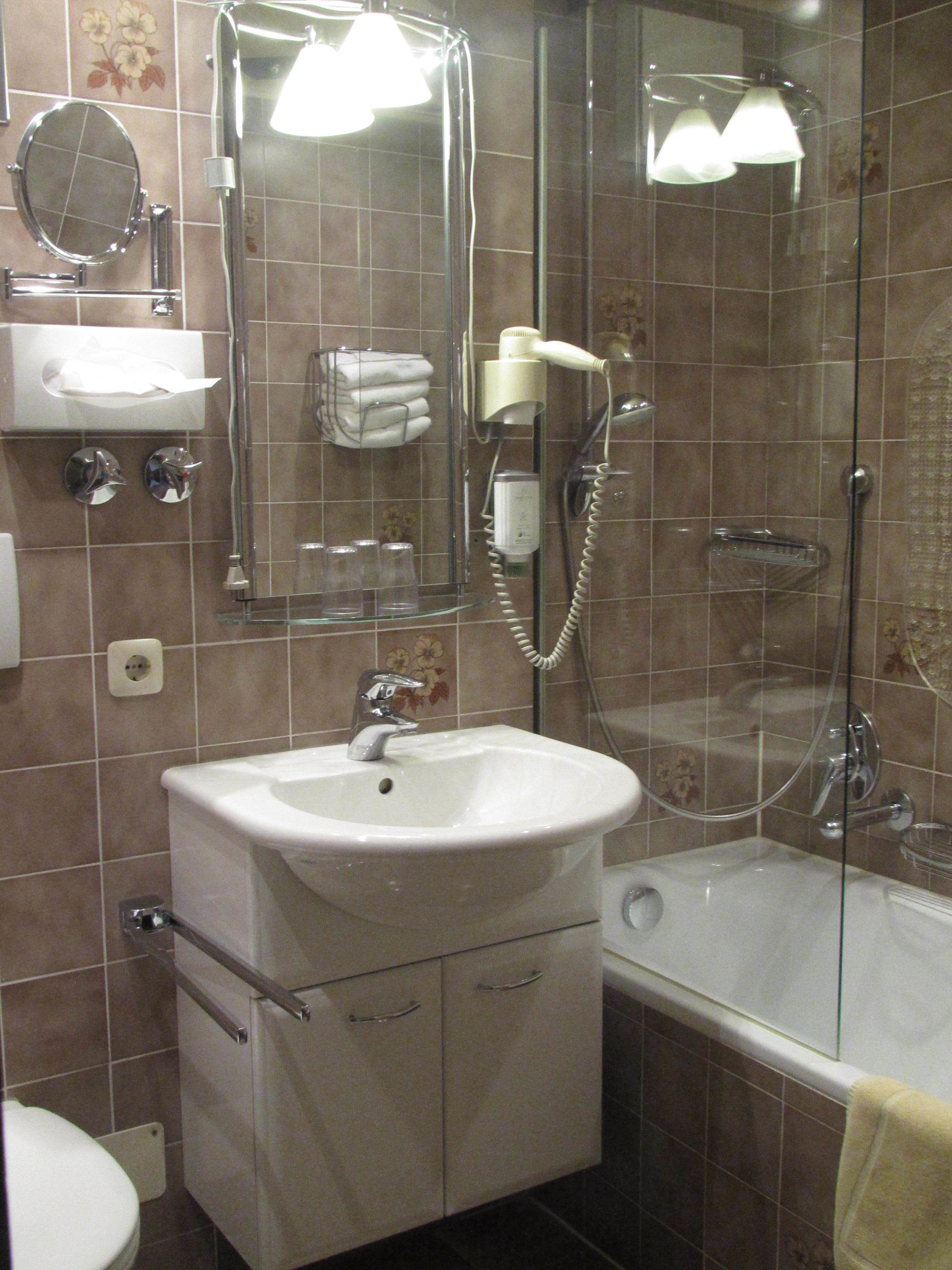 Un baño con lavamanos, espejo, toallero y zona de ducha con mampara de vidrio.